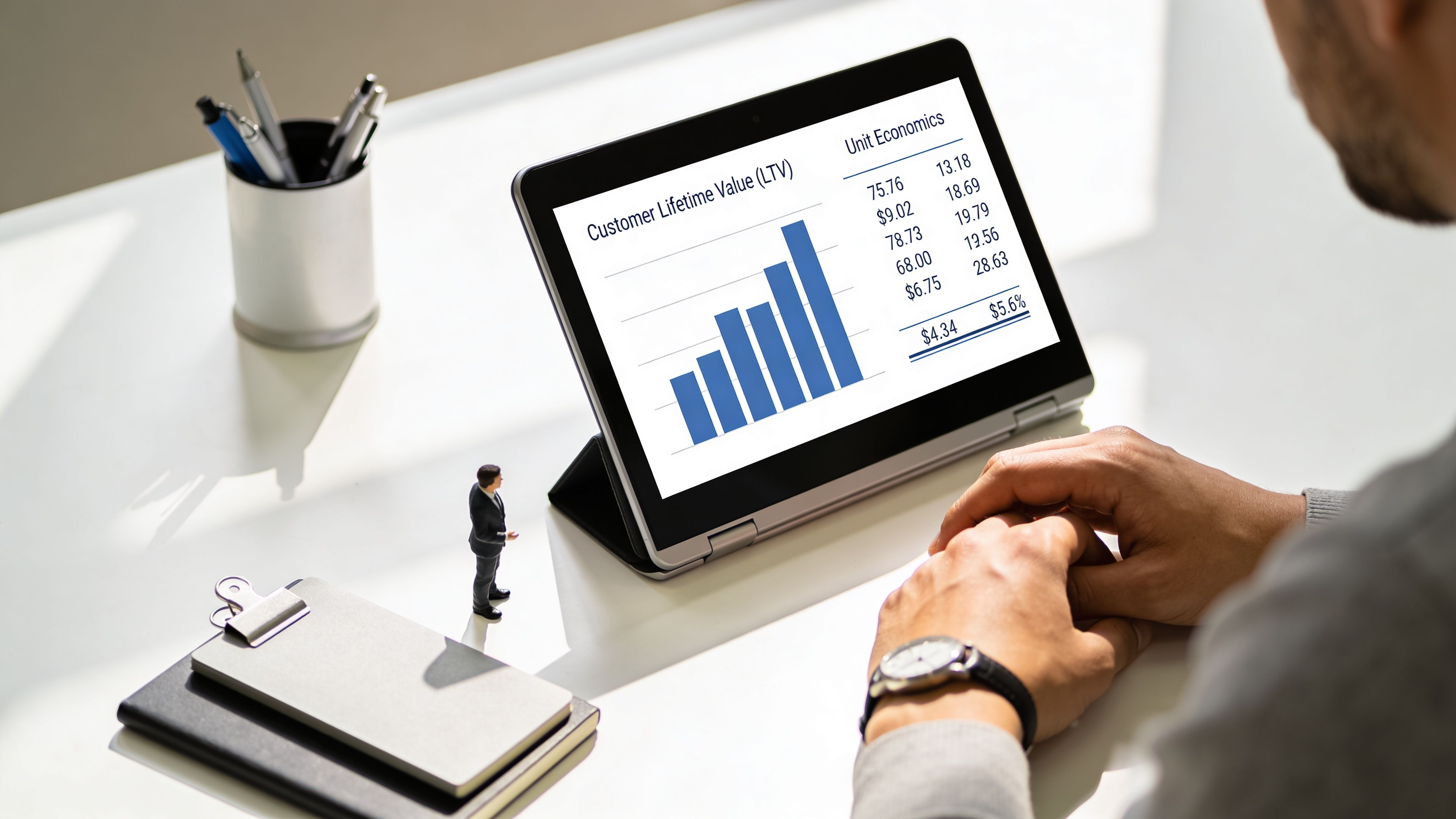 A businessman reviews data on a tablet displaying a bar chart showing customer lifetime value and unit economics.